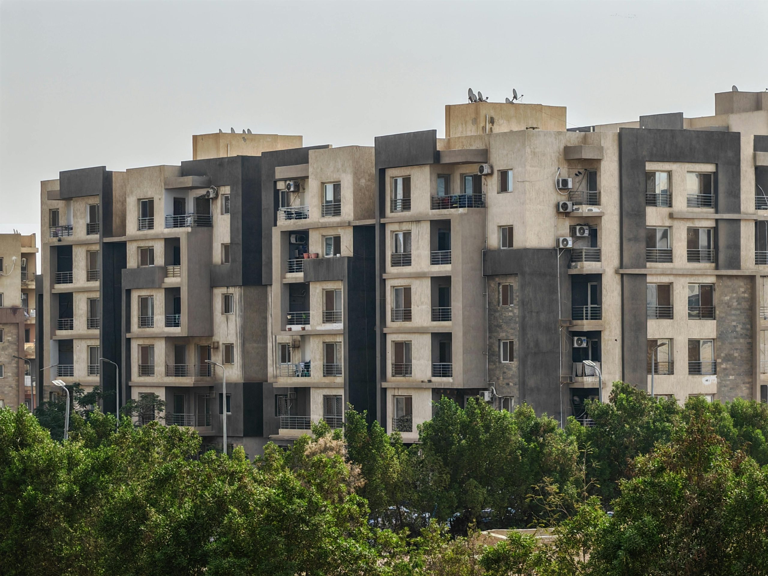 Urban residential apartment complex with trees in foreground on a clear day.